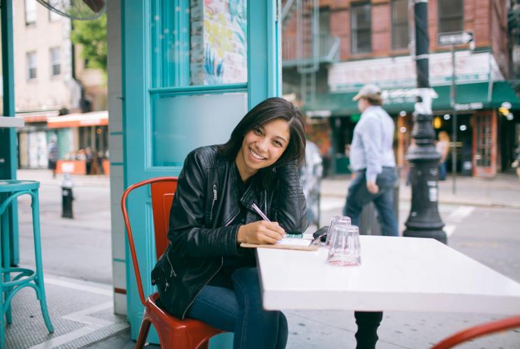 Person smiling and sitting at cafe table with pen in hand